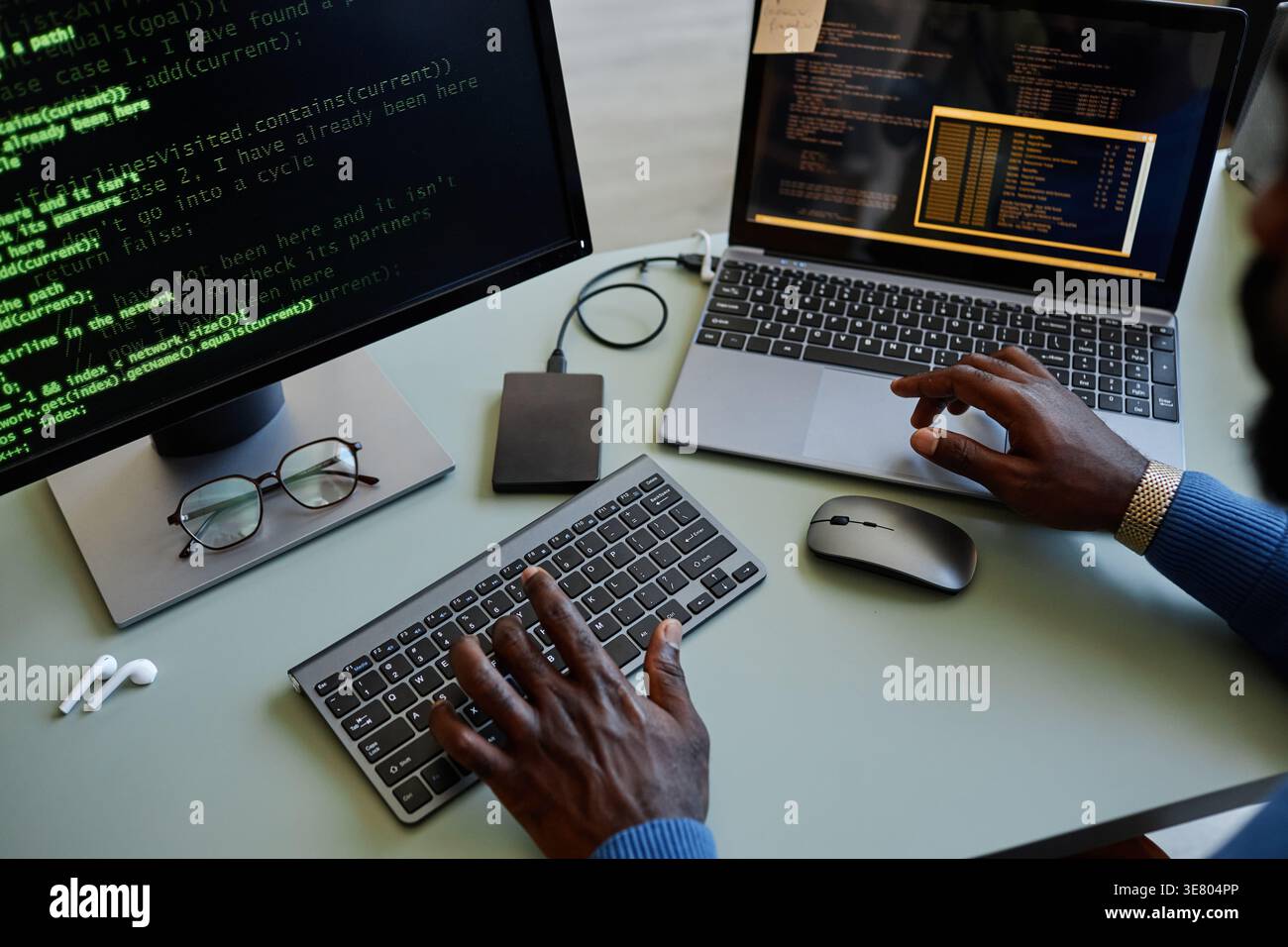 Black male programmer typing codes on computer while sitting at table with laptop in office Stock Photo