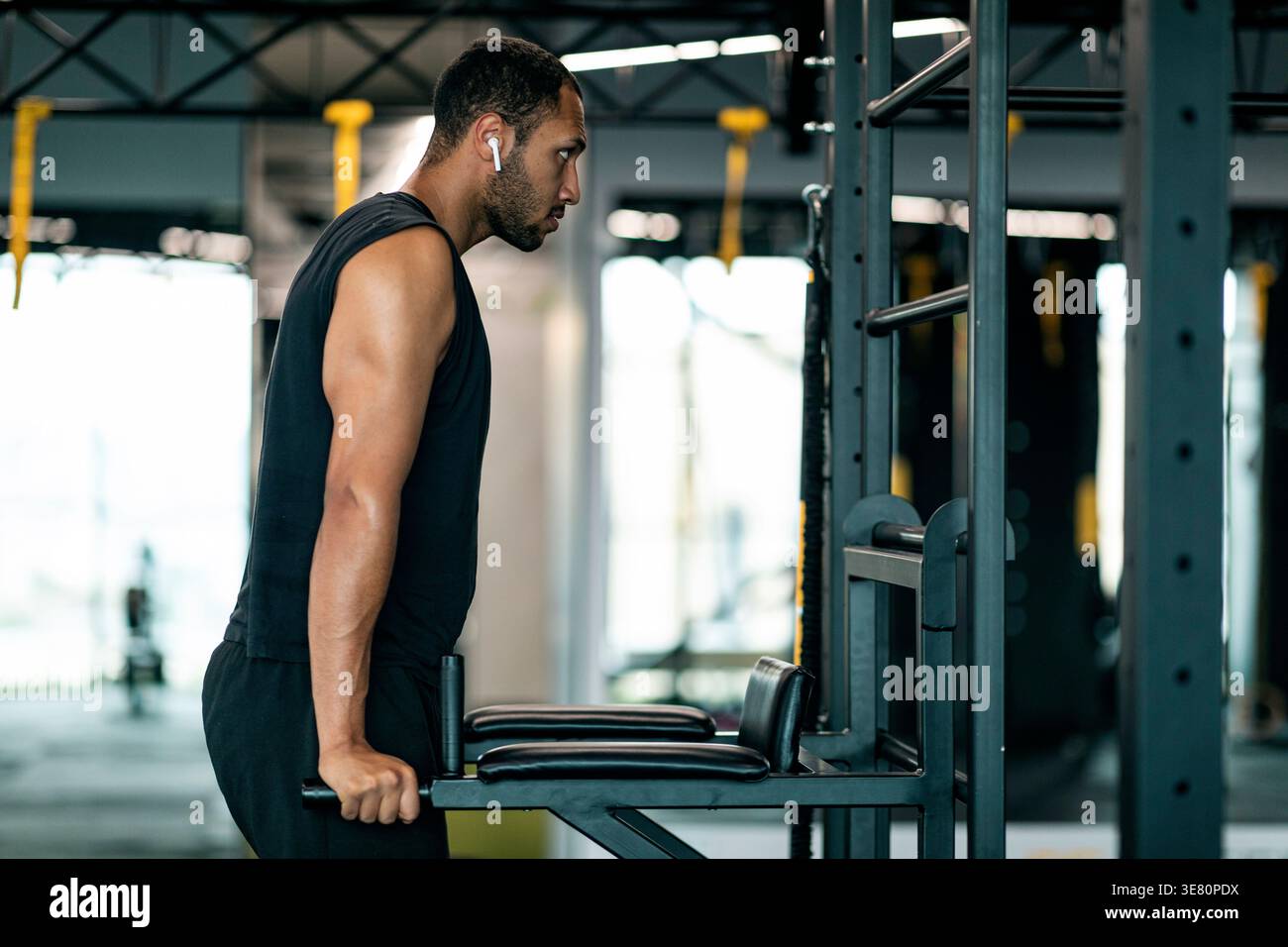 Black man with beard wearing wireless earphones doing parallel bar dips triceps exercise in gym Stock Photo