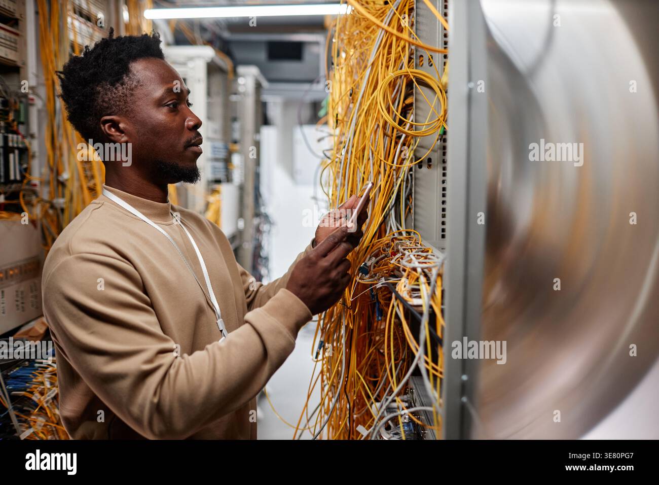 Black male system administrator setting up server and using smartphone while standing in server room Stock Photo