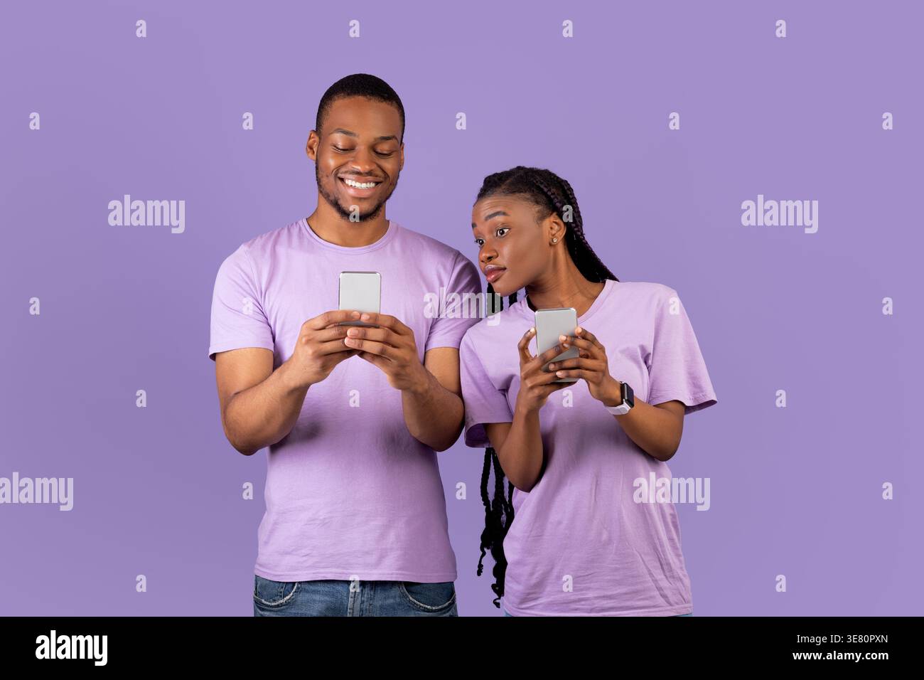 Black couple using smartphones while standing against purple background in studio Stock Photo