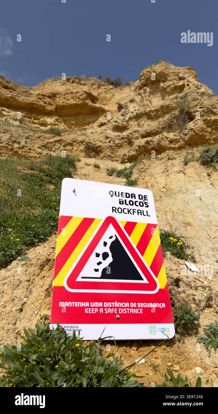 Warning sign for rockfall in English and Portuguese placed below a sandstone cliff in the Algarve region of southern Portugal Stock Photo