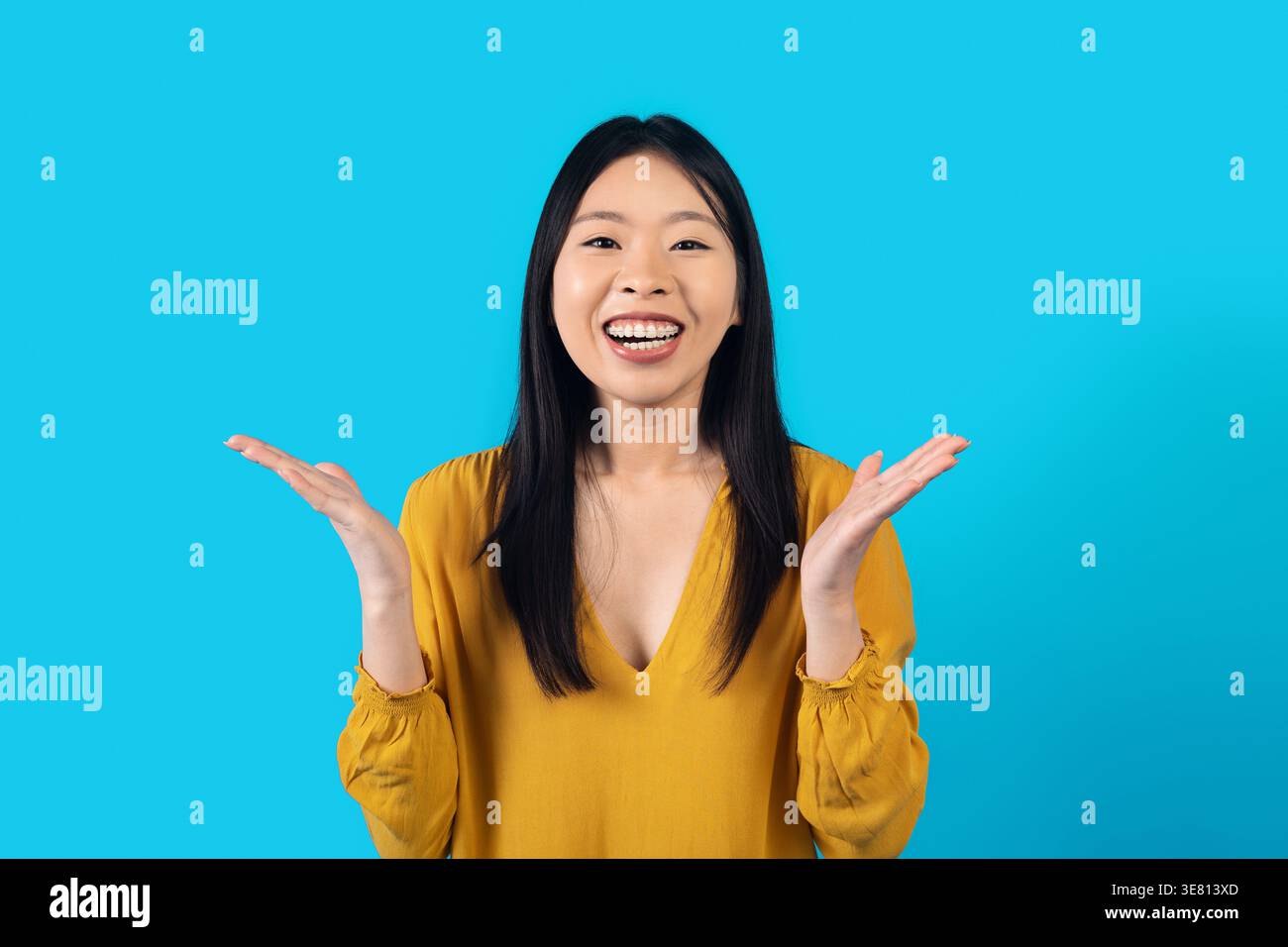 Emotional happy young pretty asian woman in yellow gesturing and laughing on blue studio background, female showing excitement. Human emotions and ges Stock Photo