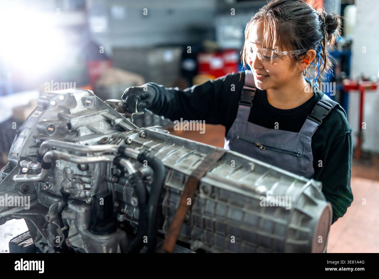 Asian female mechanic working on vehicle gearbox while standing in auto ...