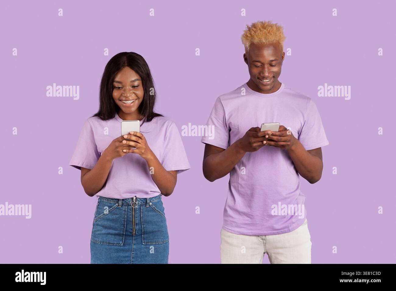 Black couple using smartphones while standing against purple background in studio Stock Photo