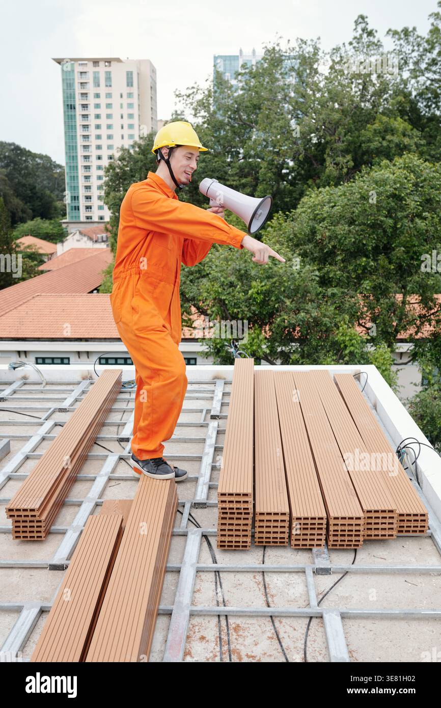 Mixed race male construction worker using megaphone looking away while standing in construction site Stock Photo