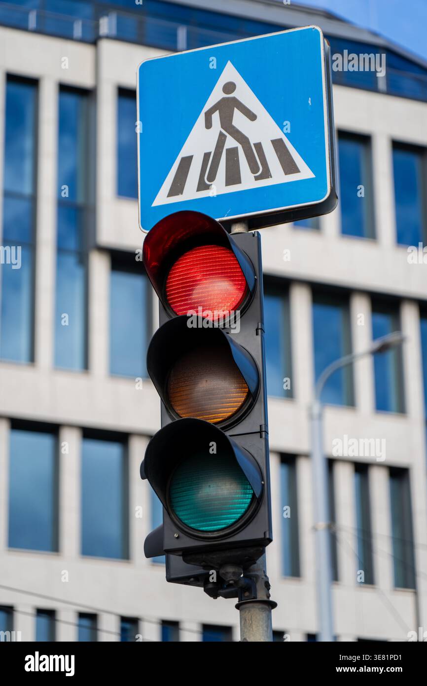 Urban traffic light showing red below a blue crosswalk sign with modern ...