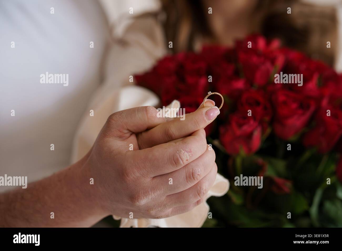 Close up of a hand presenting a sparkling diamond ring against a lush red floral background Stock Photo