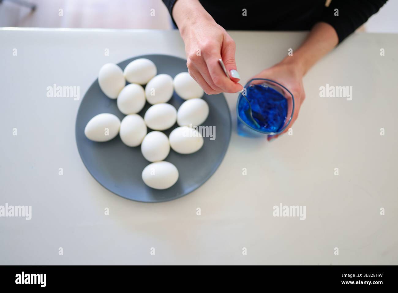 White eggs on plate and blue dye, process of coloring eggs for Easter celebration. Stock Photo
