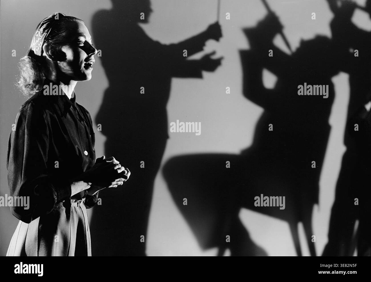 Young woman singing with hands clasped as dramatic shadows of musicians ...