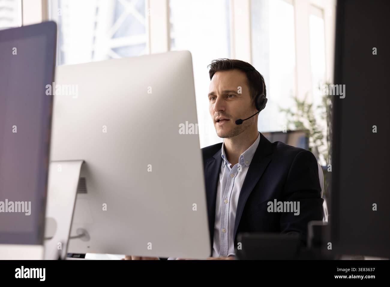 Serious businessman in headset holding conversation via videocall on pc Stock Photo