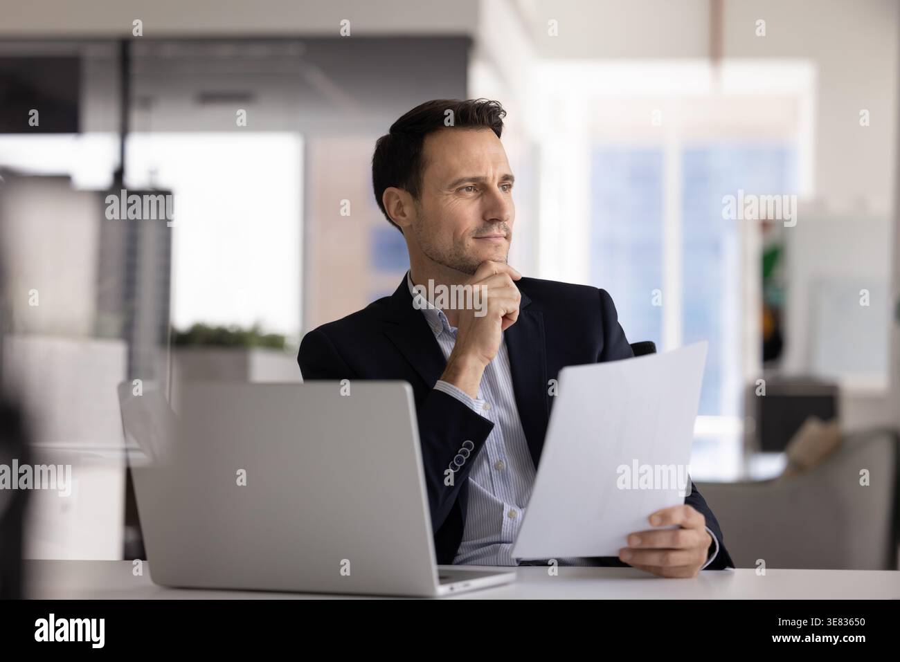 Focused Hispanic ceo using laptop printed documents at office desk Stock Photo