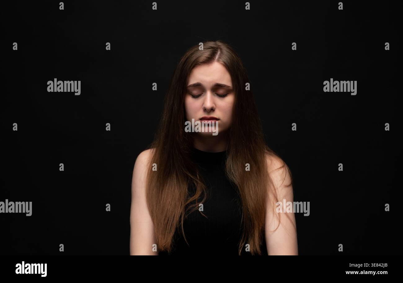 Young woman dealing with sadness, grief, depression, and mental health issues, feeling emotional with closed eyes Stock Photo