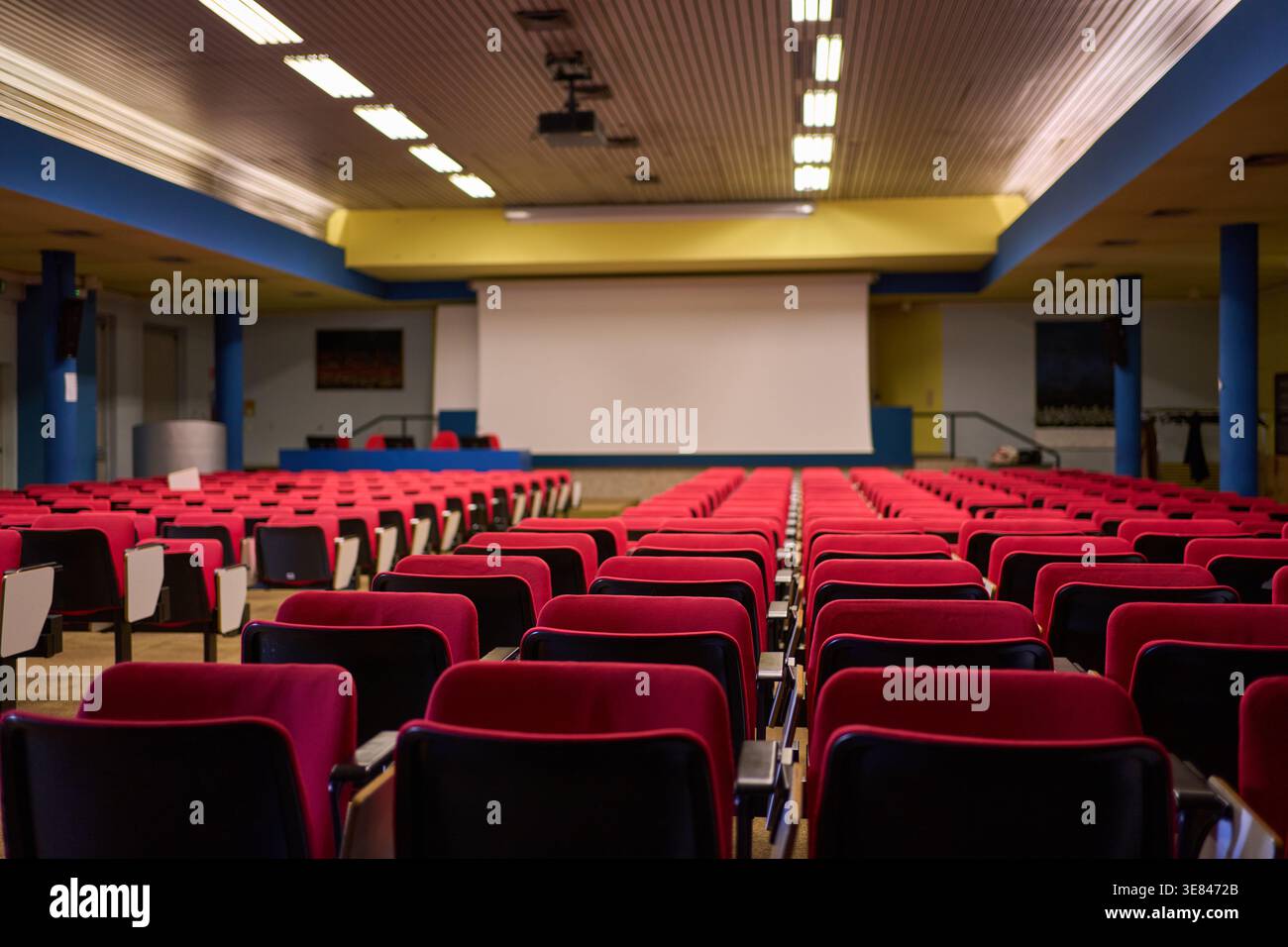 Empty conference hall or auditorium with red seats facing a projection screen, generic modern interior design. Stock Photo