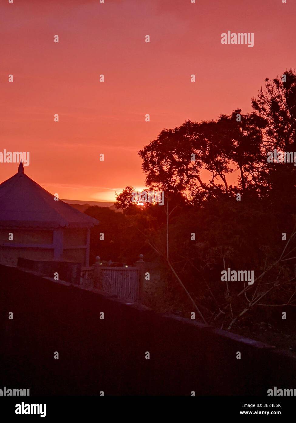 Deep Red and Orange Sunset Silhouetting Rooftop and Trees Over North Yorkshire Village, England - Smartphone Captured Stock Image