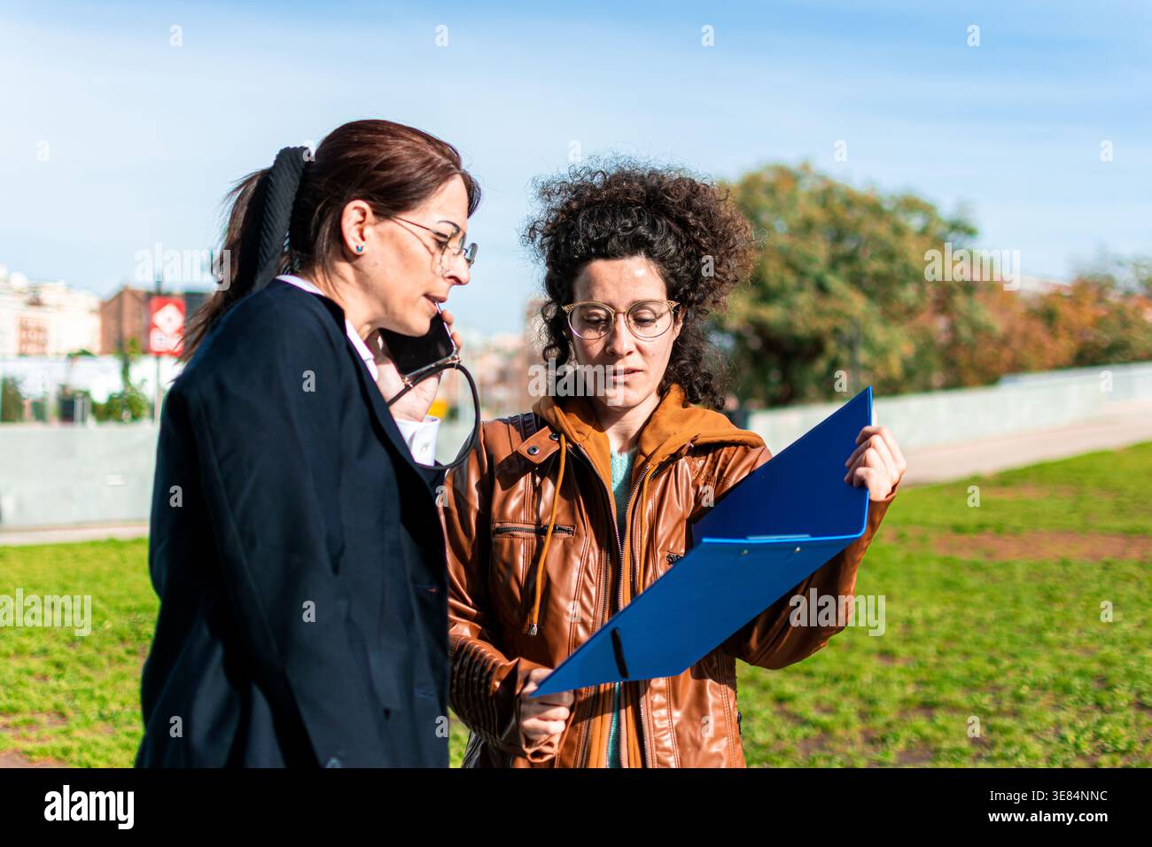 Businesswomen discussing documents outdoors while talking on phone Stock Photo