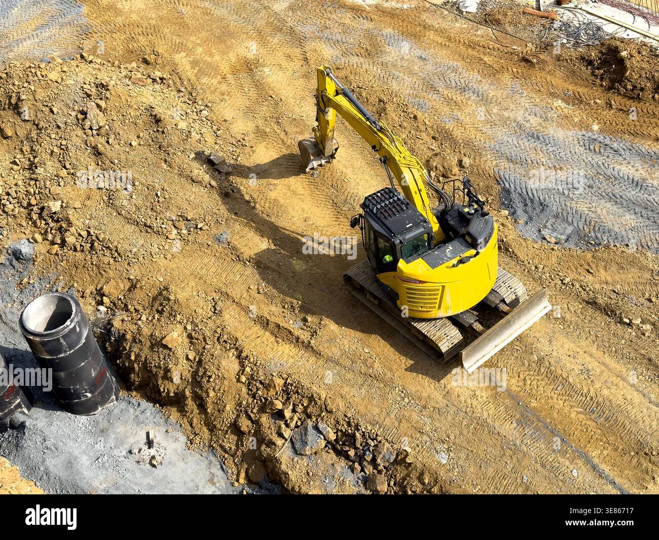 Aerial view of a yellow tracked excavator digging and grading soil for a foundation trench at an active construction site, showing earthmoving tracks Stock Photo