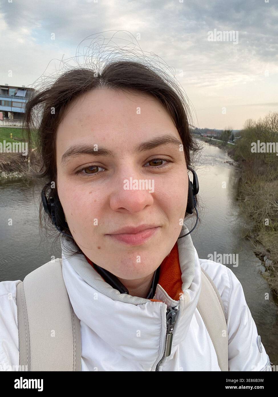 Young woman with headset taking selfie on bridge over river. Stock Photo