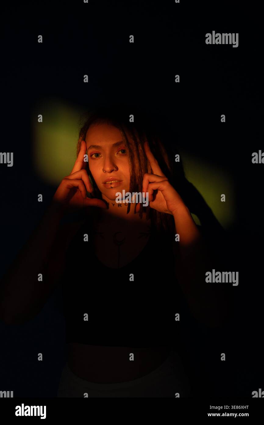 Woman with dreadlocks illuminated by dramatic lighting, creating artistic shadow play Stock Photo