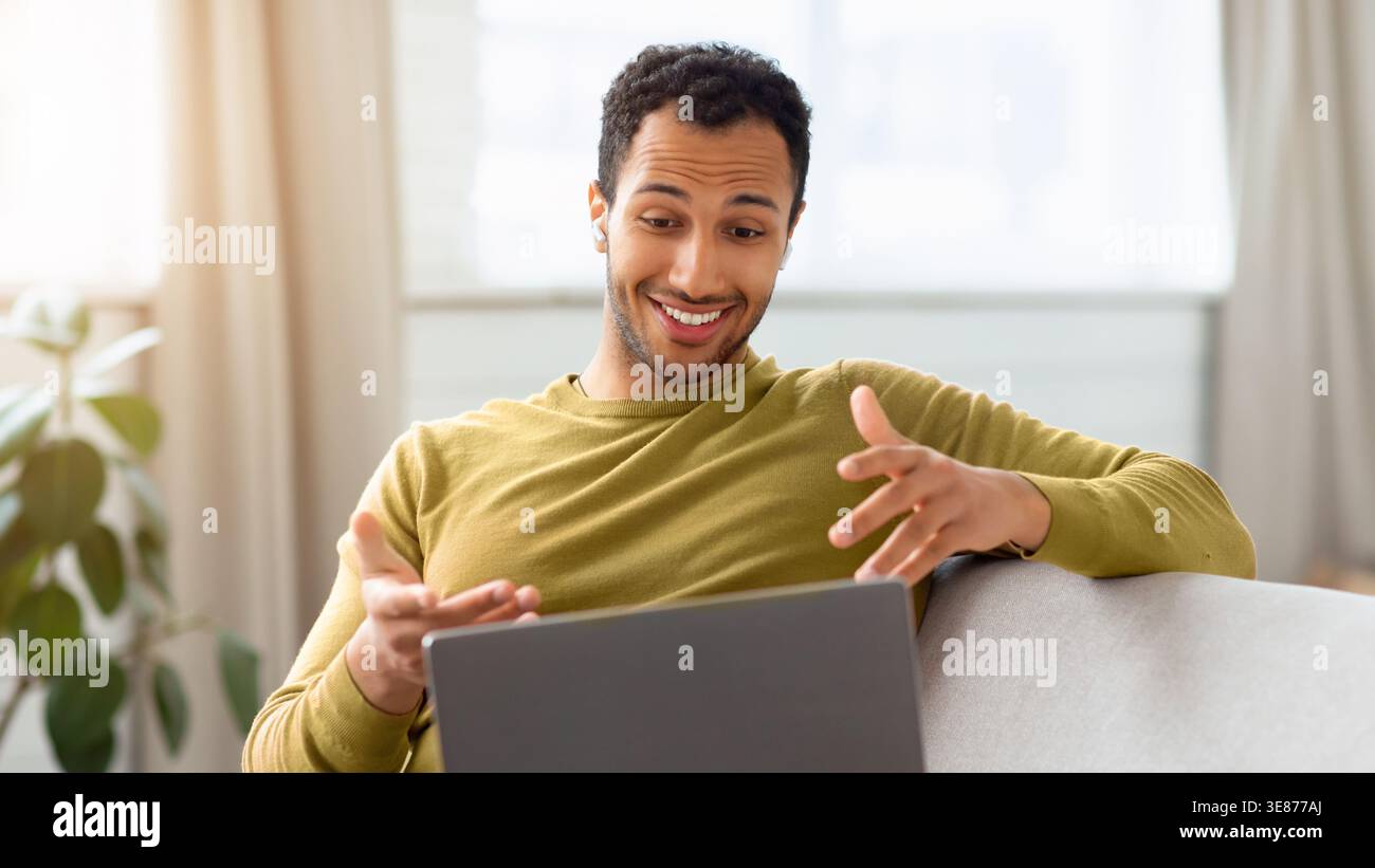 Man Sits on Sofa and Talks While Using Laptop at Home in Daylight Stock Photo