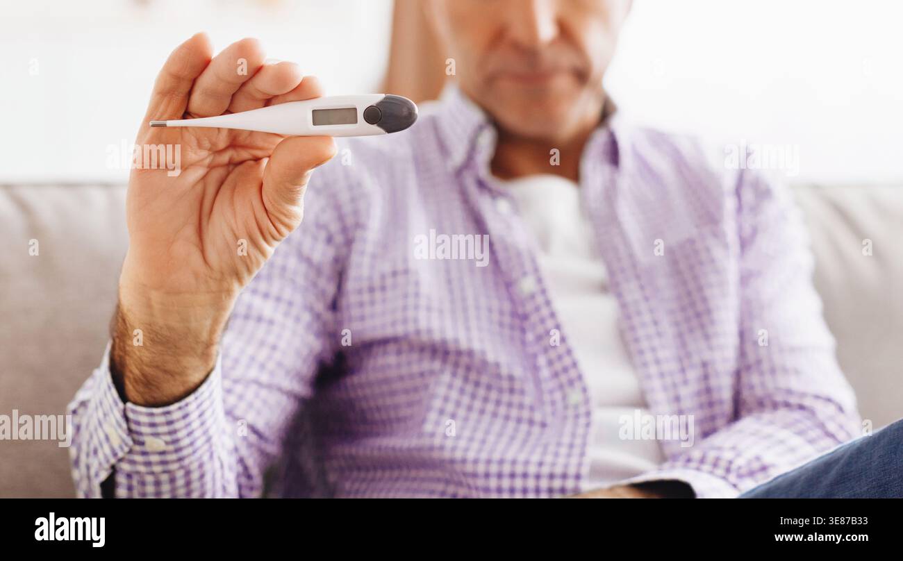 Man Measures Temperature While Sitting on Couch at Home During Daytime Stock Photo