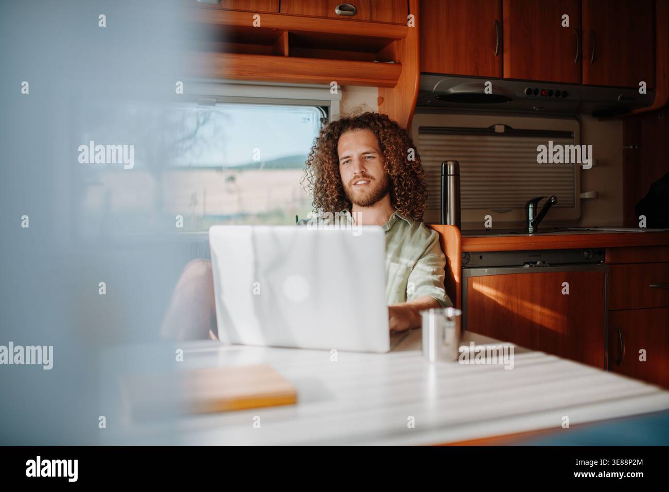 Young man working remotely from caravan. Man using camper as homeoffice, working on notebook. Stock Photo