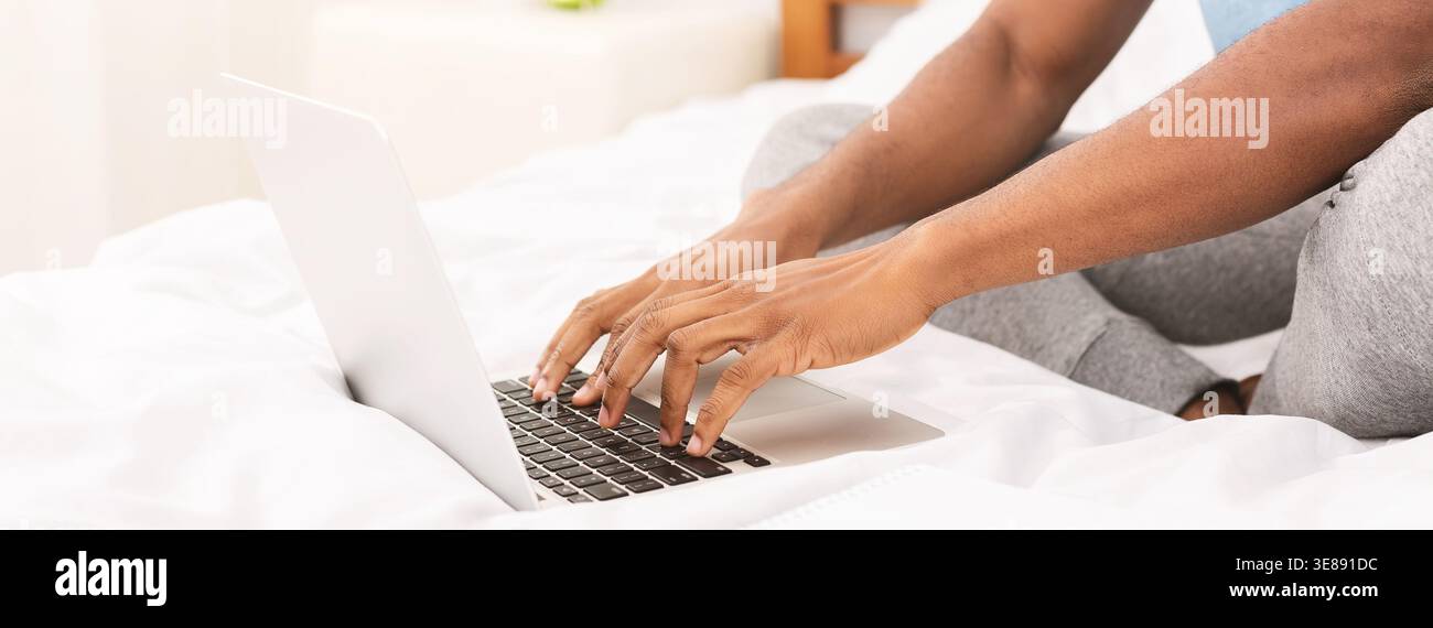 African-american programmer typing on laptop in bed Stock Photo