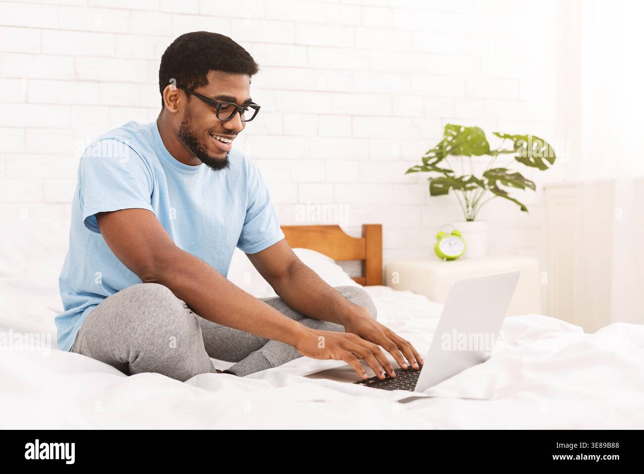 African-american programmer typing on laptop in bed Stock Photo