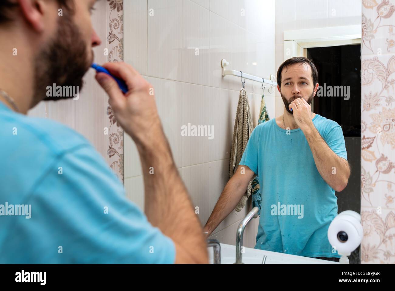 Man brushing tooth in bathroom looking at mirror reflection. Stock Photo