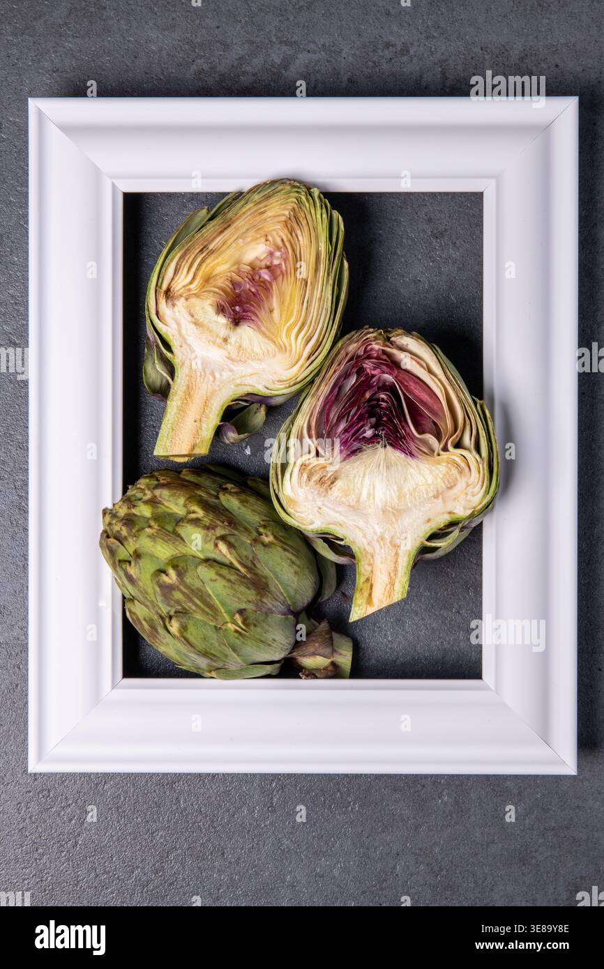 Fresh artichokes displayed in a white frame on dark surface Stock Photo