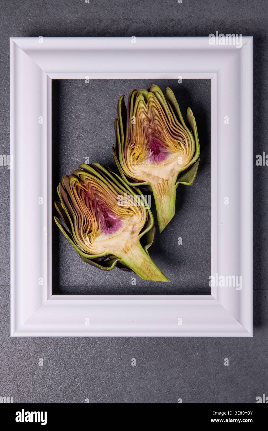 Two artichokes placed in a white frame on gray surface Stock Photo