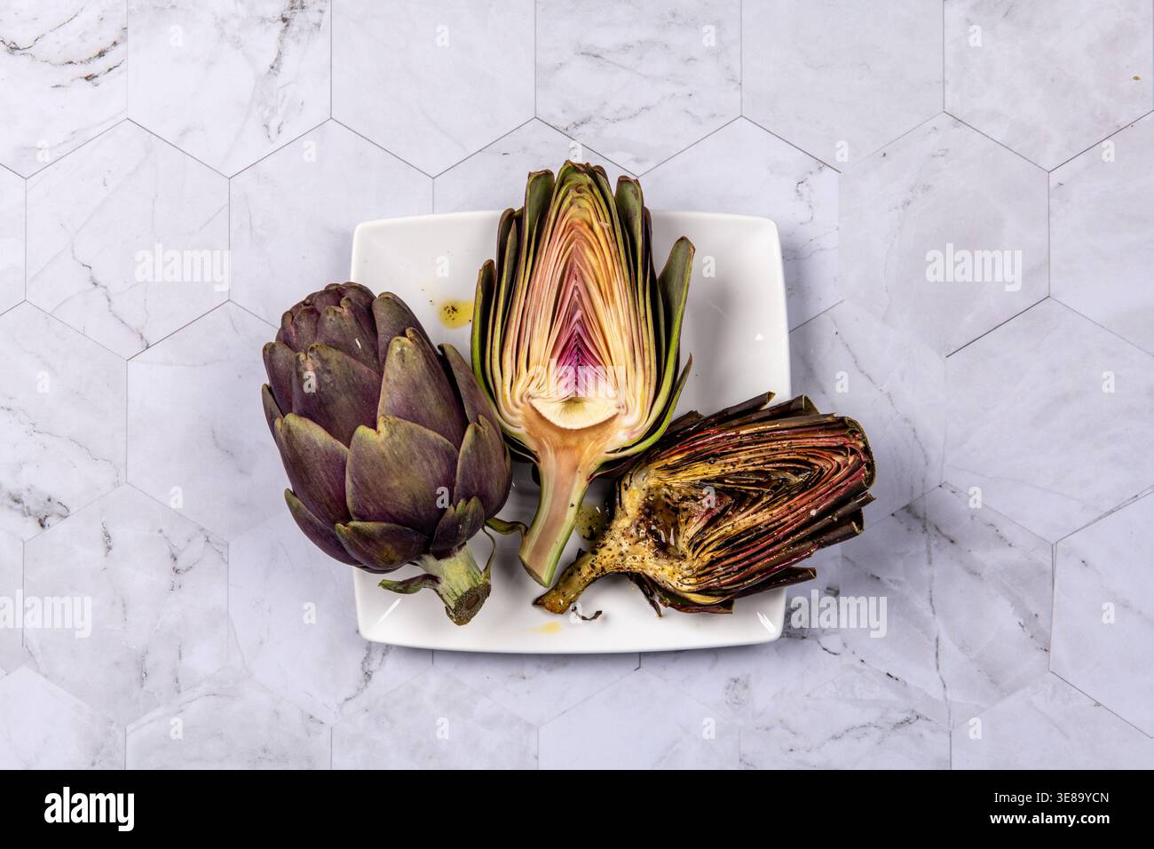 Three artichokes placed on a square plate on marble surface Stock Photo