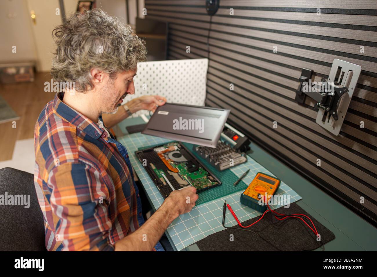 Man carefully disassembling a laptop computer, performing technical maintenance and fixing electronics on a workbench at home Stock Photo