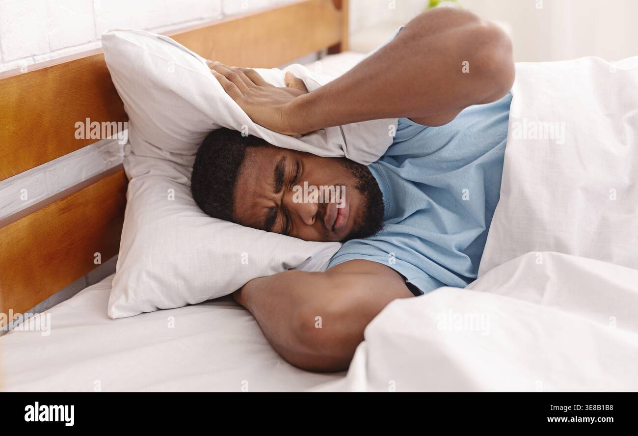 Young man in bed hiding under pillow Stock Photo