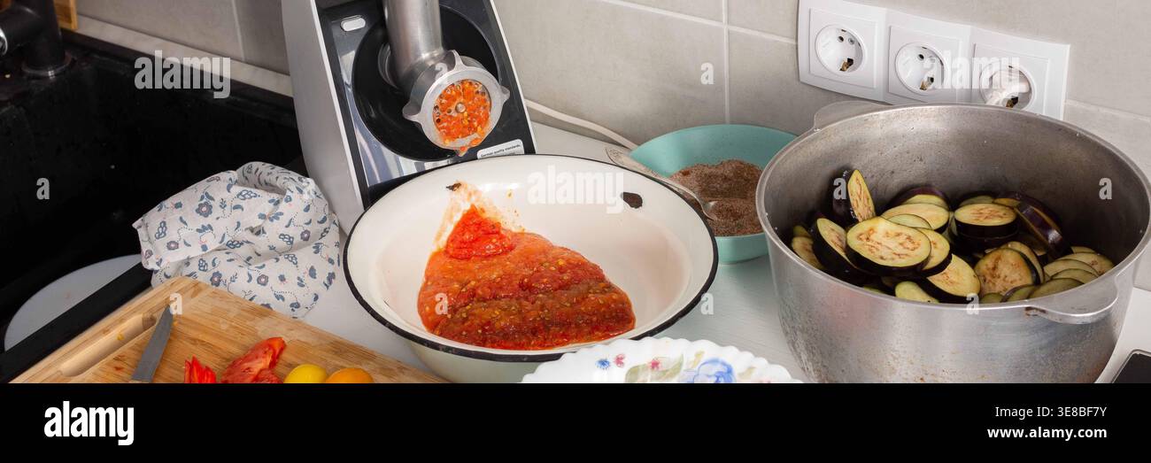 Fresh vegetables like eggplant and peppers are prepared for making eggplant caviar in a home kitchen. Various ingredients are set on the counter for t Stock Photo