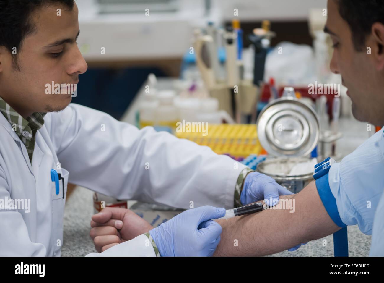 Young lab technician drawing blood from patient while doctor assists in ...