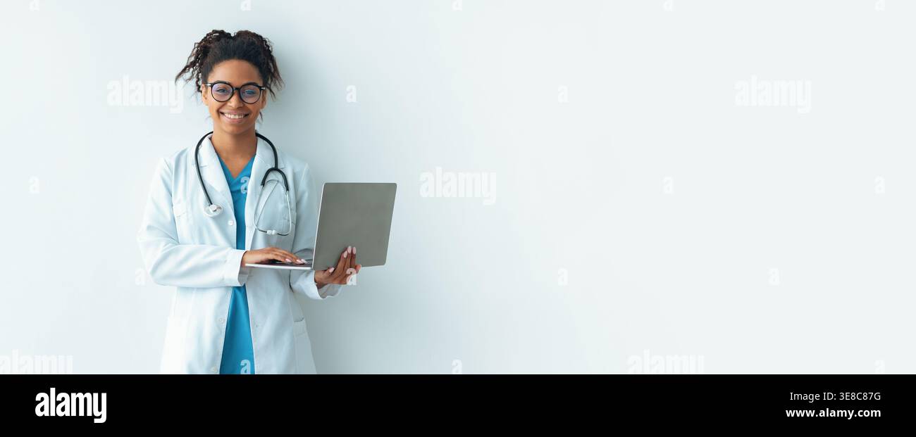 Doctor Using Laptop While Standing Against Plain Wall in Medical Setting Stock Photo