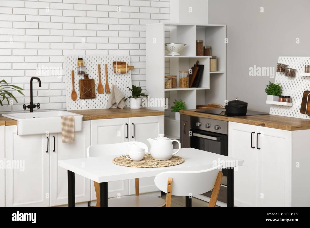 Stylish light kitchen with pegboards and modern dining table Stock Photo