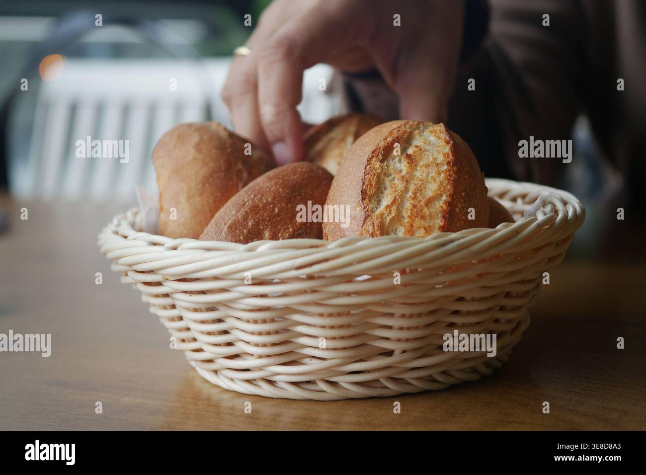 Hand reaches for bread in a basket on a table Stock Photo
