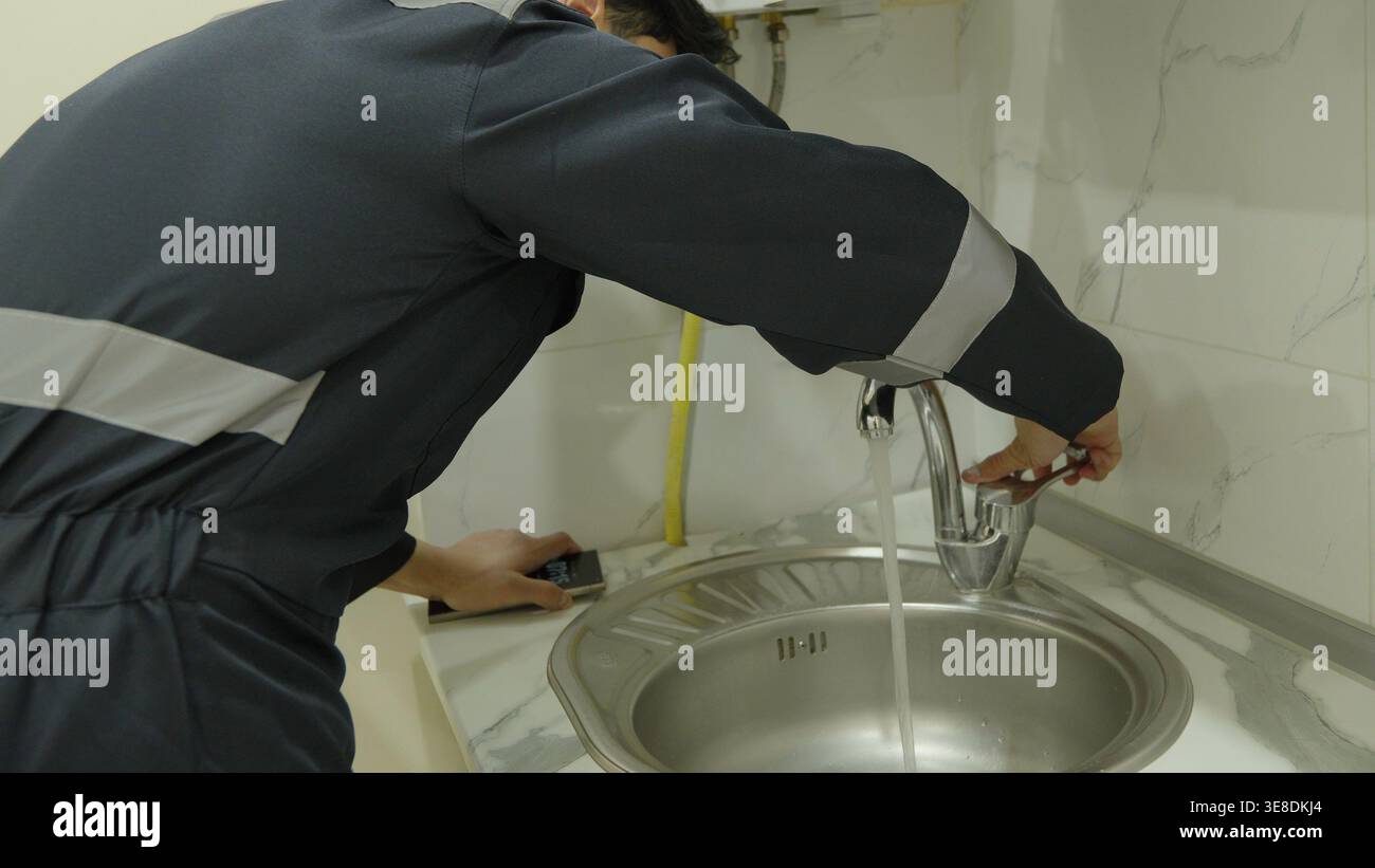 Professional plumber repairing a sink faucet in kitchen Stock Photo