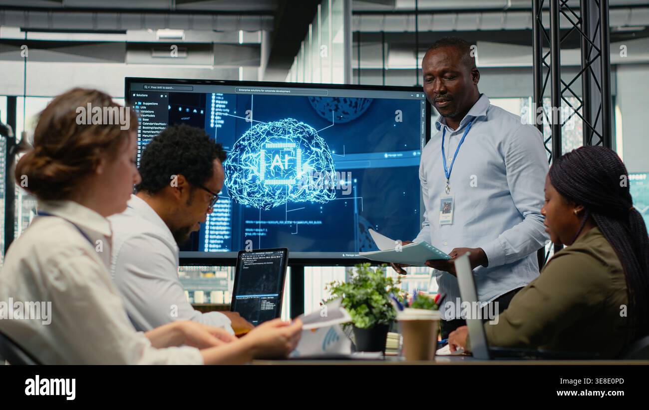Programmer gives presentation to executives, implementing AI chatbot reducing work volume. Startup office IT expert analyzing business insights for management using artificial intelligence, camera B Stock Photo