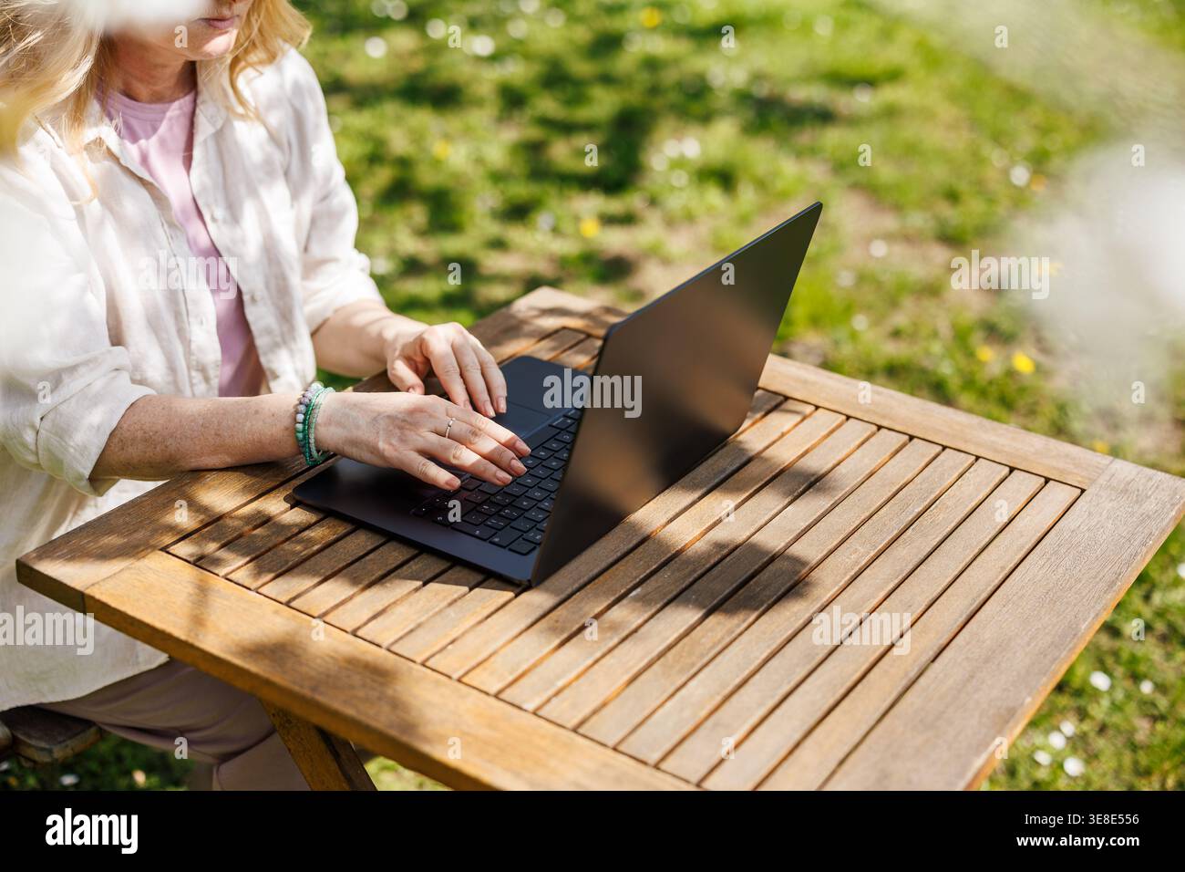 Freelancer working on laptop in spring garden. Woman using computer at outdoor desk in backyard. Remote work from home in sunny day Stock Photo