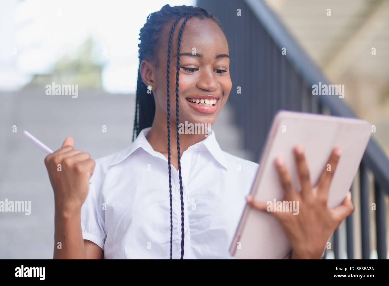 Happy young Black woman celebrating while holding tablet and stylus on stairs. Achievement, success, online learning, business progress, digital produ Stock Photo