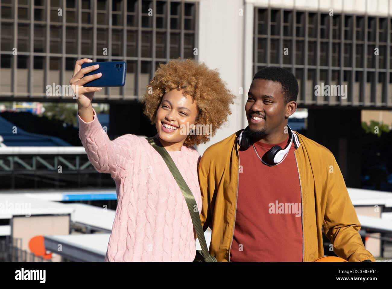 African American couple taking selfie with smartphone on rooftop near office tower with basketball. Urban, outdoor, sunny, candid, duo, smiling, terrace Stock Photo