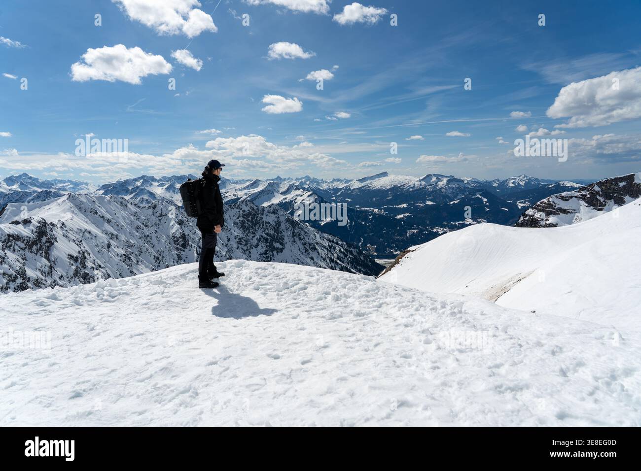 Hiker standing on snowy mountain ridge under dramatic clouds Stock Photo
