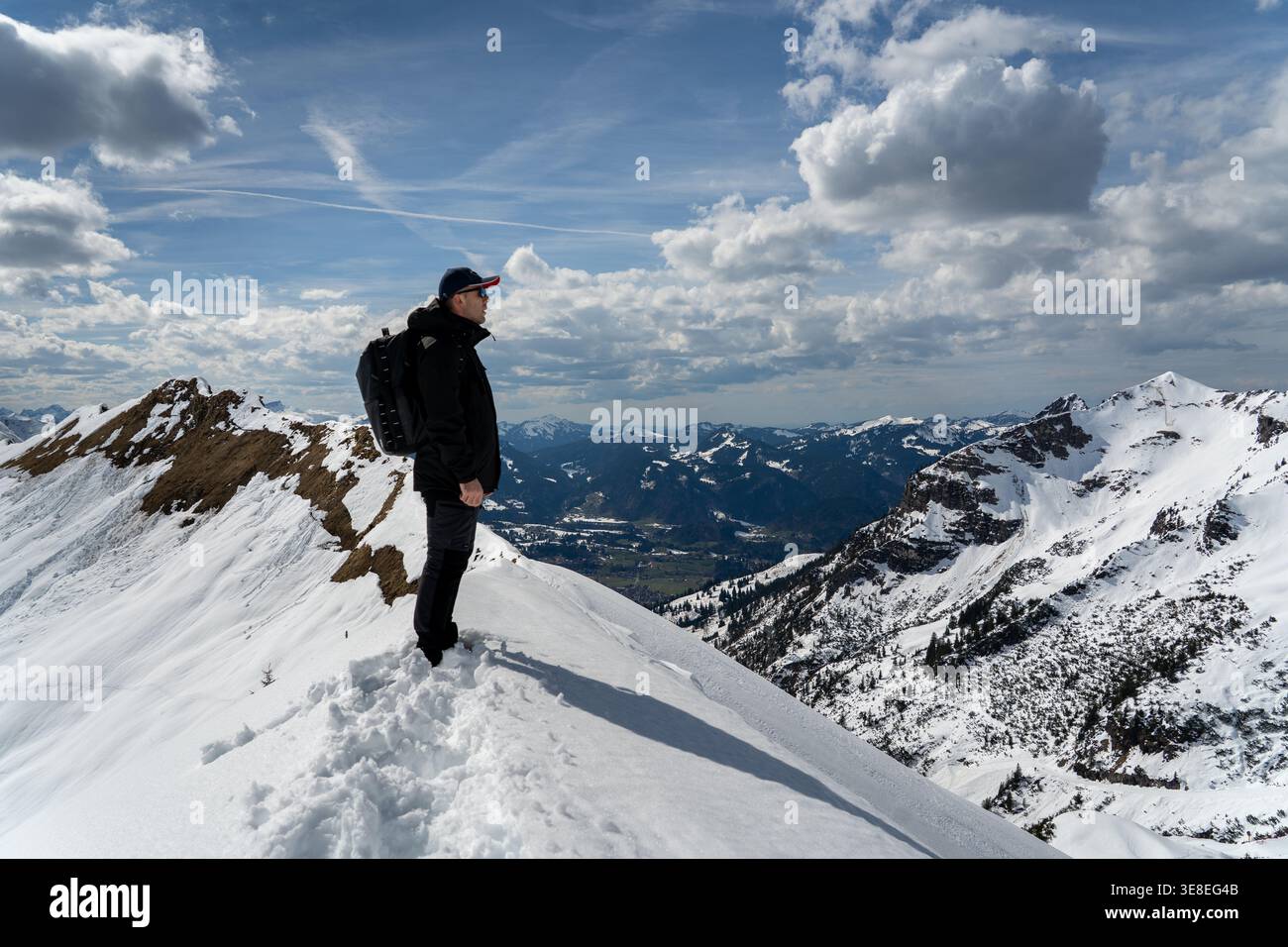 Hiker standing on snowy mountain ridge under dramatic clouds Stock Photo