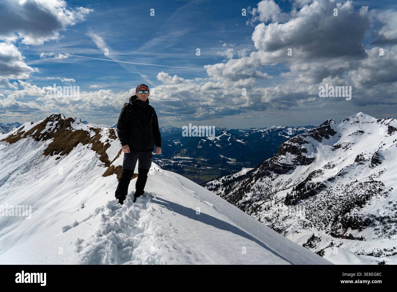 Hiker standing on snowy mountain ridge under dramatic clouds Stock Photo