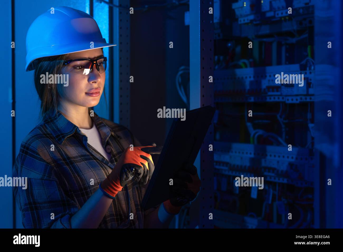 Female electrician inspecting electrical system using tablet device. Engineering diagnostics. Stock Photo