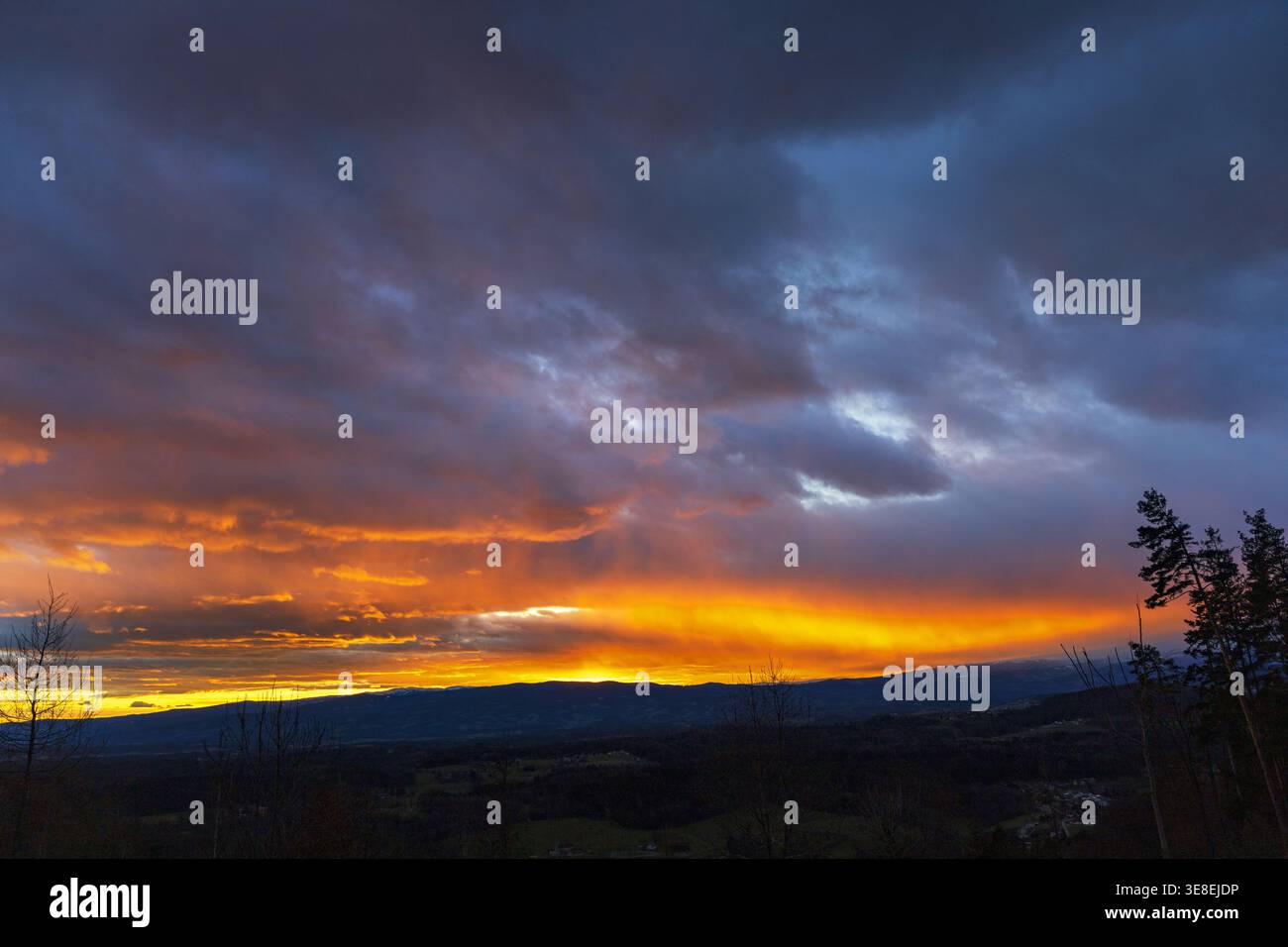 Beautiful sunset with glowing horizon and dramatic clouds over landscape. Stock Photo