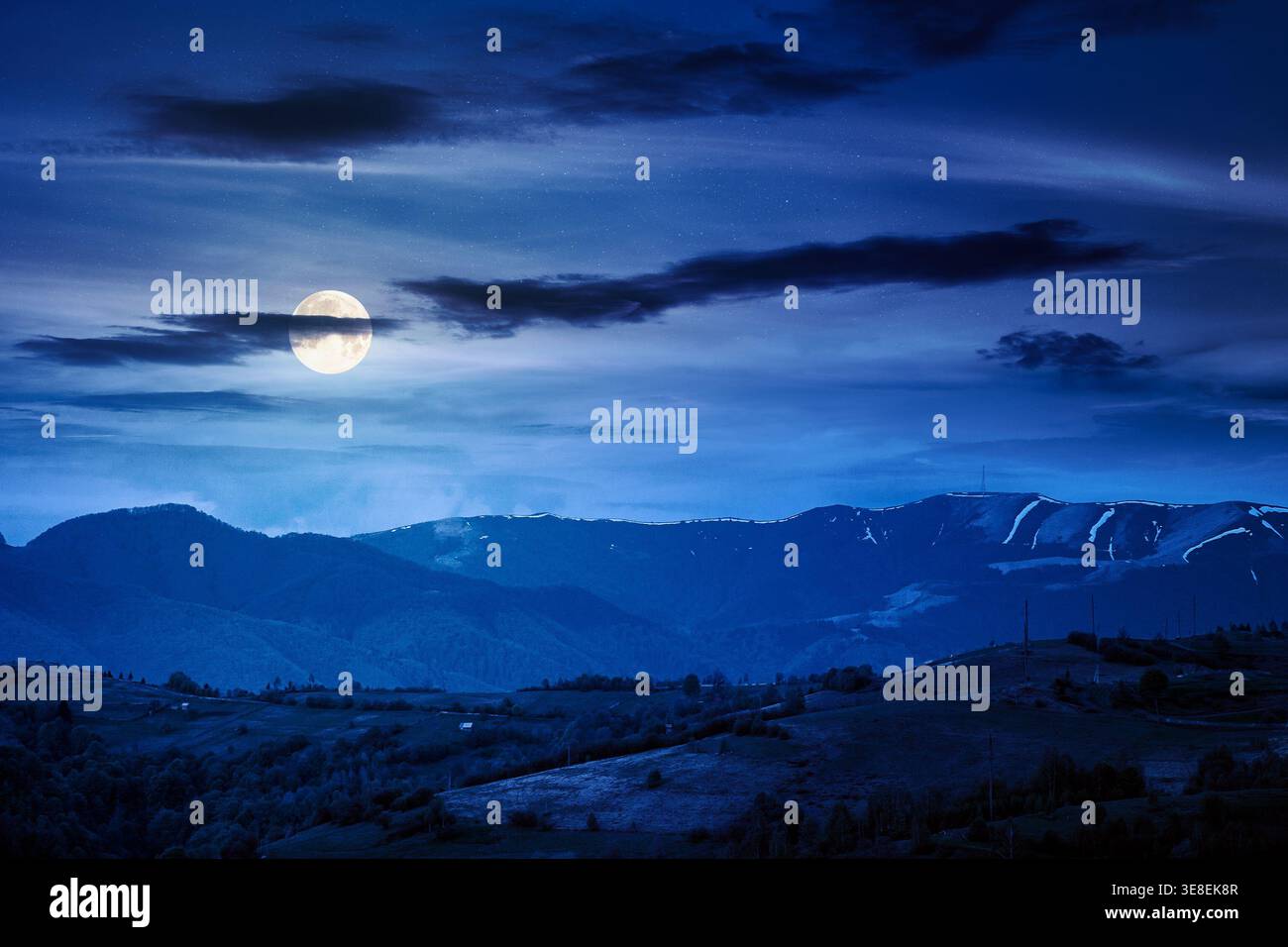 mountainous countryside scenery at night. mysterious sky above the distant valley and ridge. full moon over remote meadows and trees on rolling hills. Stock Photo