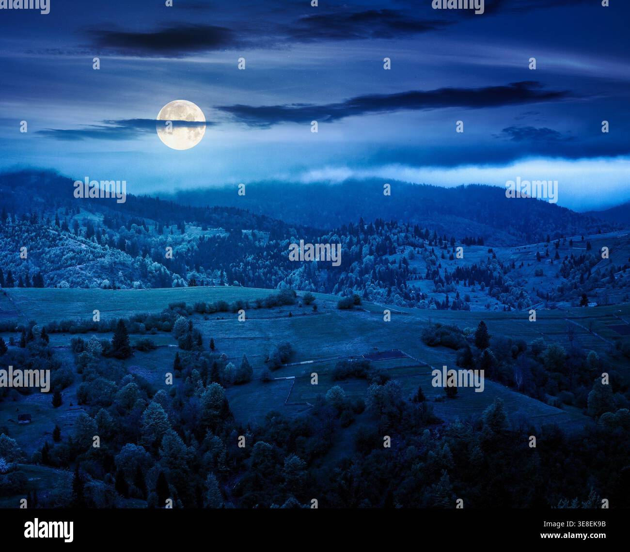 rural mountain landscape during spring at night. wonderful countryside scenery on a cold weather in full moon light. cloudy sky above rolling hills in Stock Photo
